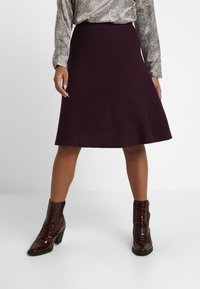 Mörkröd utsvängd kjol i mjukt tyg, kombinerad med glansiga bruna ankelskor med krokodiltextur och klack.