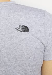 Šedé bavlněné tričko s krátkým rukávem, s černě potištěným logem "The North Face" na horní části zad. Texturovaná tkanina.