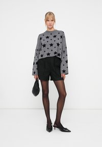 Gray sweater with black star pattern, paired with textured black shorts, sheer black tights, black heeled shoes, and a black handbag.