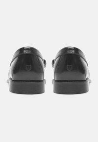 Chaussures en cuir noir avec une finition brillante, bout arrondi et petit talon empilé. Présentent des coutures discrètes et un emblème de logo à l'arrière.