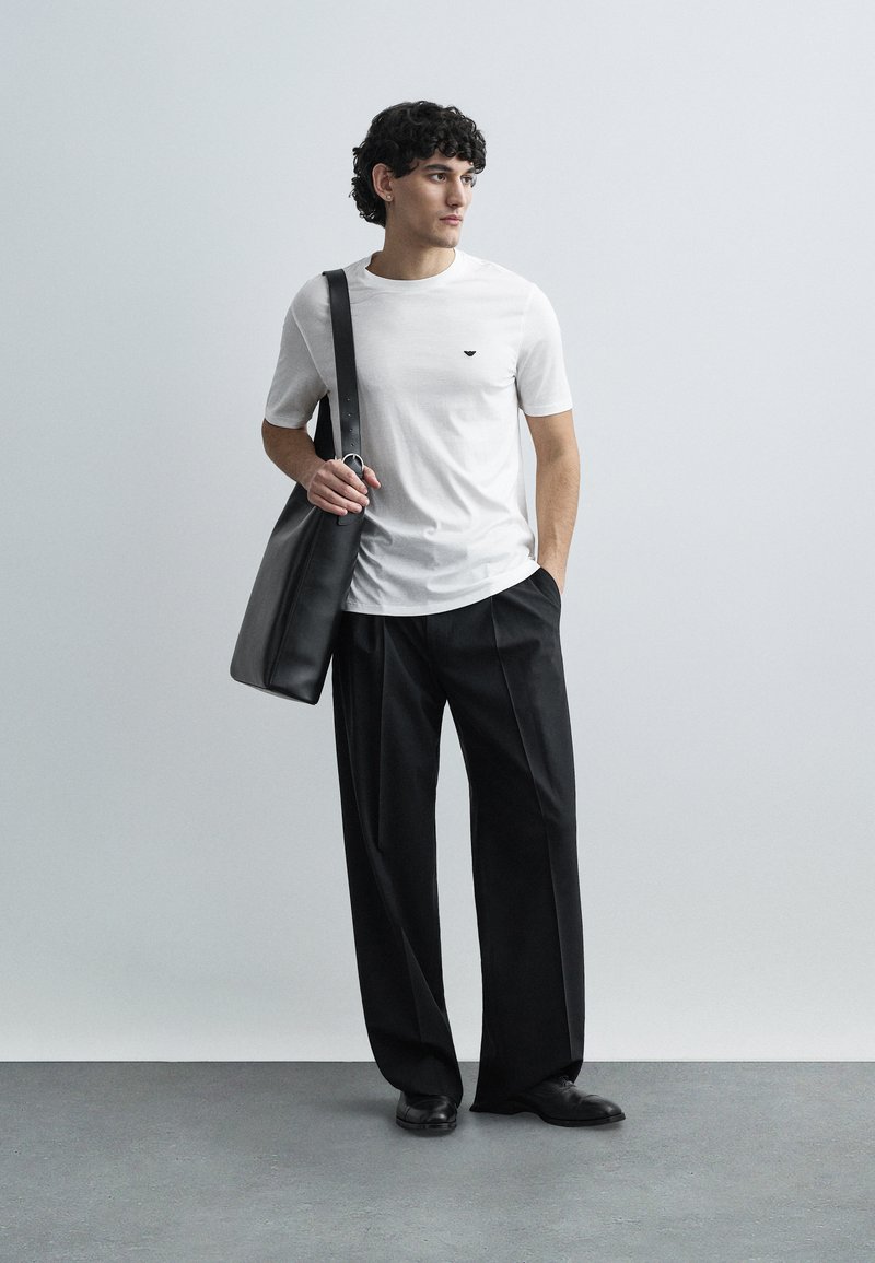 Maglietta bianca a maniche corte con un piccolo logo nero, abbinata a pantaloni neri larghi e a una borsa a tracolla in pelle nera.