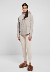 Lys grå fleece pullover med høj krave, frontlomme, parret med beige leggings og brune pels slippers.