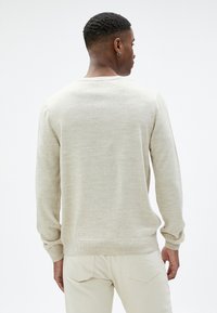 Beżowy, lekki sweter z długimi rękawami, okrągłym dekoltem oraz ściągaczami przy mankietach i dolnej krawędzi. Miękka tekstura, prosty design i minimalne detale.