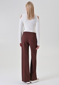 Witte gebreide trui met open schouders en een zachte structuur, gecombineerd met hooggesneden, wijdvallende donkerbruine broek en witte sneakers.