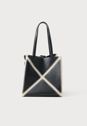 Black leather tote bag with cream stitching creating an X pattern. Features two black handles and an unstructured shape.