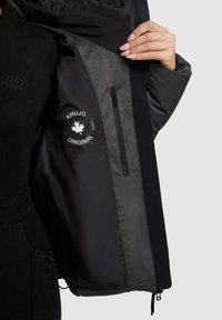 Interno della giacca nera e grigia con tasca con zip; presenta il logo "KHUJO ORIGINAL", texture liscia e pannelli in tessuto contrastanti.