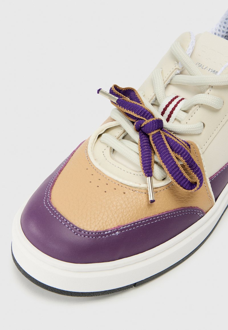 Baskets marron, violettes et crème avec cuir texturé, bout arrondi, lacets violets et éléments en métal argenté. Semelle en caoutchouc blanc avec motifs.