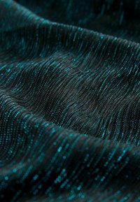 Krupni plan tamne tkanine s teksturiranom, valovitom površinom koja sadrži sjajne, tirkizne metalne niti tkanjene u vertikalnim linijama.