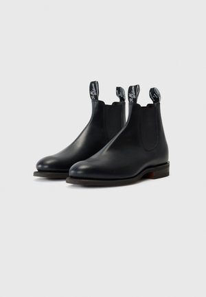 Botas Chelsea de cuero negro con paneles laterales elásticos, costuras en contraste y tiradores con el logo de la marca. Suelas planas de goma.