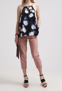 Fladdrande svart topp med vita och blå blommönster, i kombination med ljusrosa cropped-byxor. Svarta sandaletter med remmar och en mörk väska.