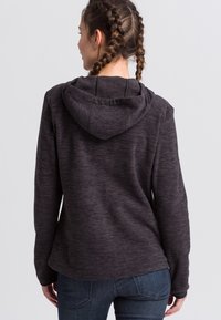 Mørkegrå hættetrøje med en struktureret overflade, der har snøre i hætten og lange ærmer, sammen med mørke denimjeans.