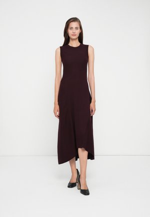 Abito midi senza maniche di colore bordeaux con corpino aderente, orlo asimmetrico e tessuto testurizzato. Abbinato a scarpe con tacco alto nere.