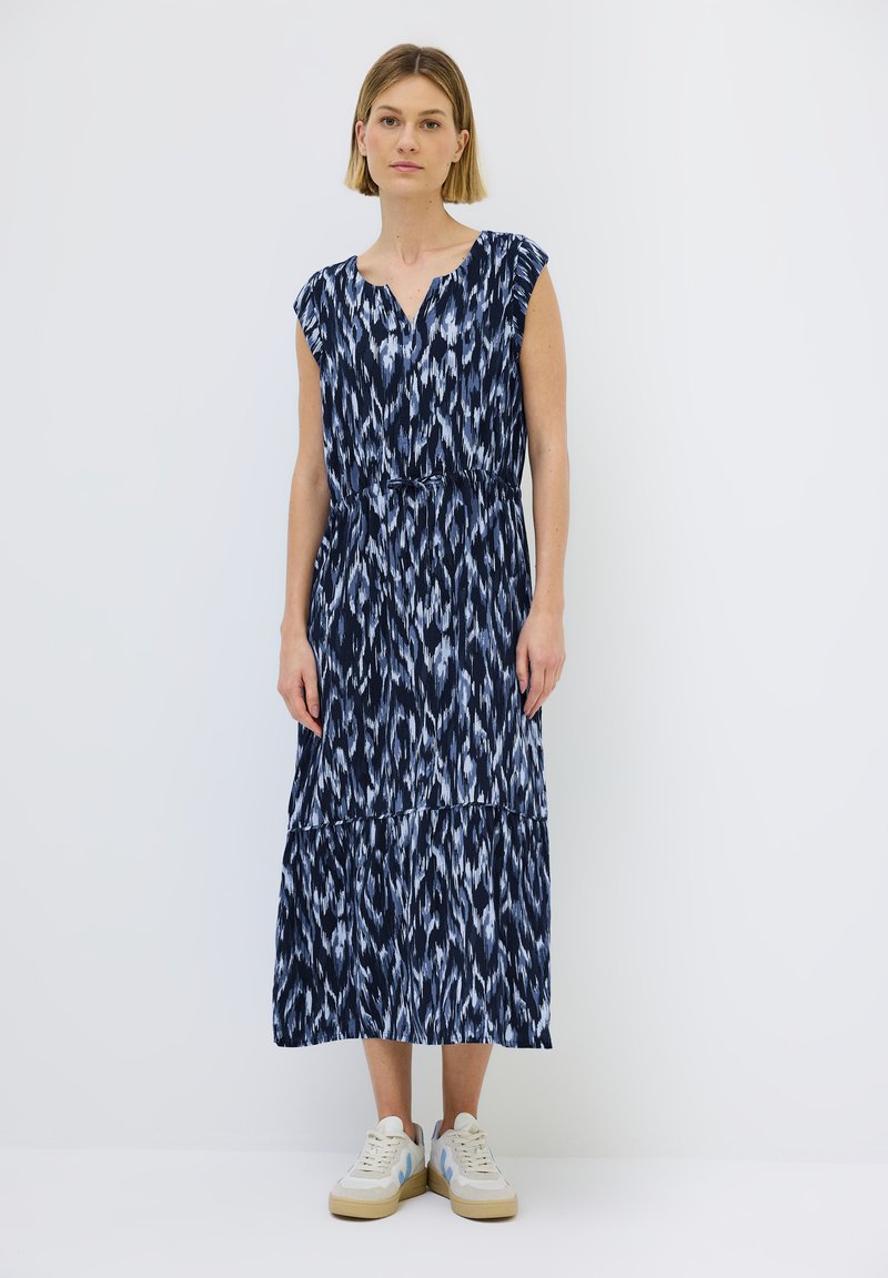 Navyblaues Maxikleid mit schichtweise gestaltetem Design, das ein abstraktes Muster in Hellblau und Weiß zeigt, sowie einem verstellbaren Taillenbund. Getragen mit weißen Sneakers.