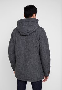 Chaqueta de plumas gris y texturizada con capucha, cuenta con detalles de botones en las mangas y un logotipo en la parte superior de la espalda.