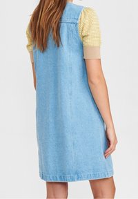 Denimkleid in Hellblau mit geradem Schnitt, ausgestattet mit einem Oberteil aus strukturiertem gelbem Stoff mit kurzen Puffärmeln. Einfache Nähte und keine sichtbaren Verschlüsse.