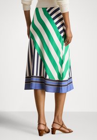 Saia às riscas com riscas verdes e azul-marinho marcantes e uma bainha azul, feita de tecido liso. Acompanhada por sandálias de salto castanhas.