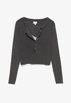 Chemise grise à manches longues et cropped, en tissu côtelé, avec un plastron à boutons, un détail en dentelle au niveau du col, et une couche blanche visible en dessous.