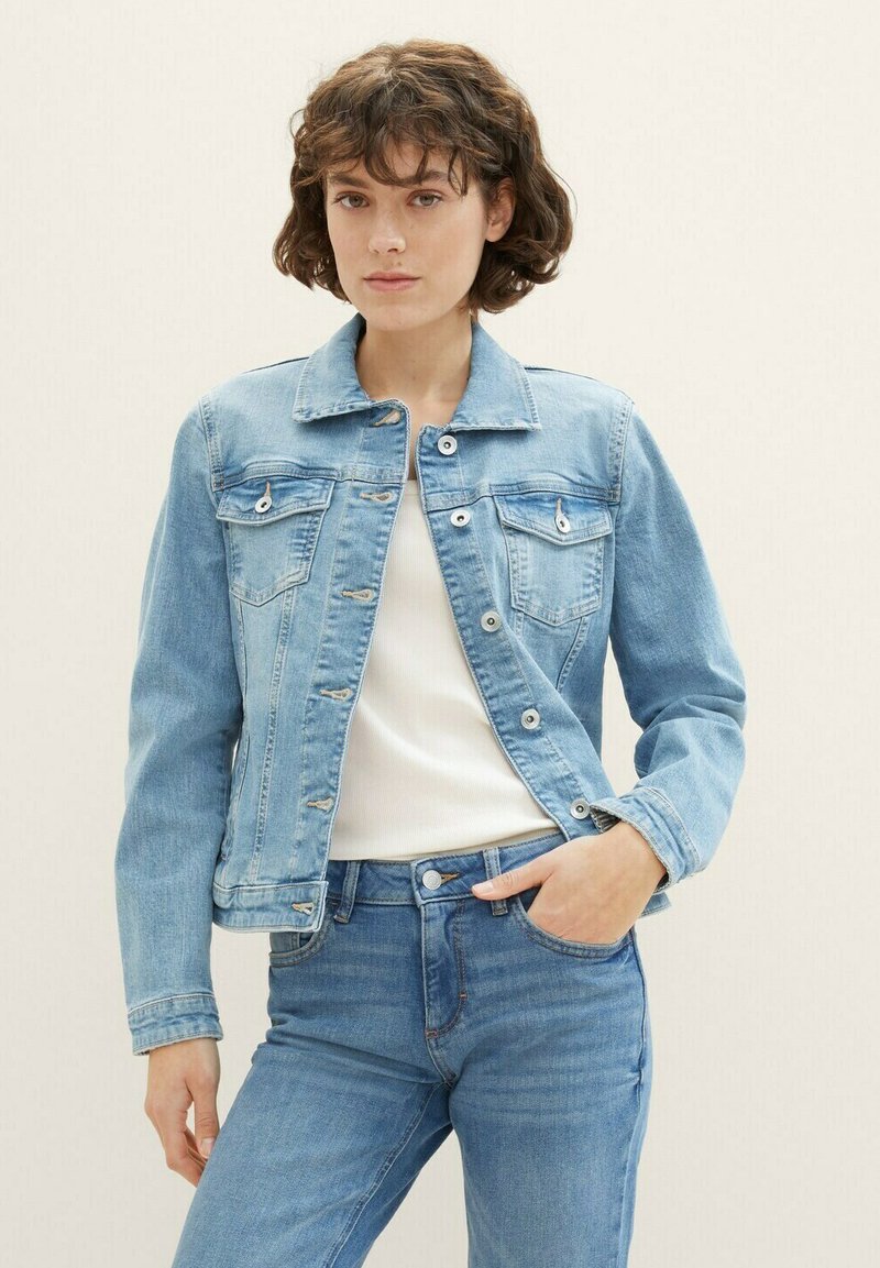 Svetlo modra denim jakna z dolgimi rokavi, z gumbi na pritisak, dvema žepoma na prsih in klasičnim ovratnikom, kombinirana s kremno majico in modrimi kavbojkami.