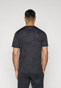 Μαύρο αθλητικό T-shirt με υφασμένη καμουφλάζ υφή, κοντά μανίκια και στρογγυλή λαιμόκοψη. Λογότυπο στο κέντρο της πλάτης.