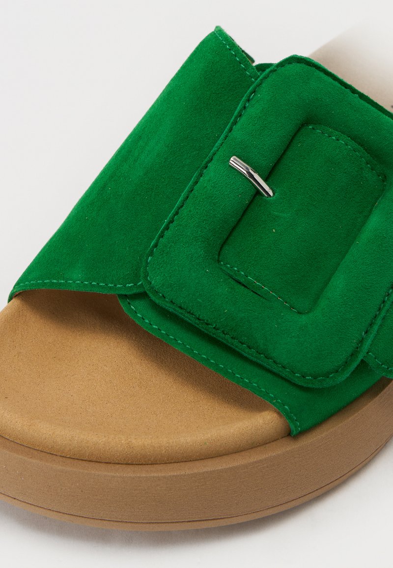 Grüne Wildledersandalen mit quadratischer Schnalle, leichte Gummisohle in Tan und weicher Textur. Glatte Oberfläche und kräftige Farbakzente.