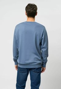 Svetloplava crew neck pulover z dolgimi rokavi, gladka tekstura, rebrasti manšeti in rob. Priložnostni fit, oblečen z temnoplavimi džinsom.