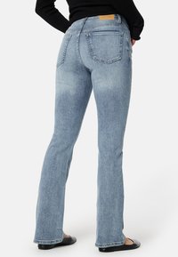 Hellblaue Denim-Jeans mit einer taillierten Silhouette, ausgestellten Beinen und Gesäßtaschen. Mit einem braunen Leder-Patch am Bund.