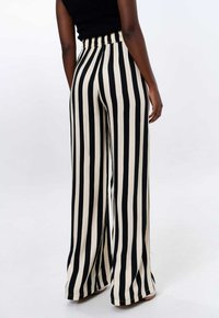 Zwarte en crème brede broek met verticale strepen, een elastische tailleband en een lichte, vloeiende stof die elegant valt.