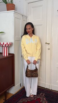 Femme en sweat à capuche jaune GAP et pantalon de survêtement blanc tenant un sac à main à motif léopard, debout à l'intérieur près d'une porte blanche et d'une armoire.