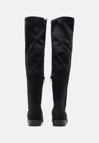 Botas negras hasta la rodilla con parte superior de tela suave y tacón de ante. Detalles de cremallera en el lateral que aportan practicidad y un toque de diseño.