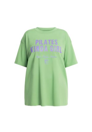 T-shirt verde chiaro oversize con scritta viola "PILATES KINDA GIRL" e una piccola illustrazione di bevanda sotto.