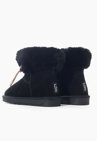 Stivali alla caviglia in suede nero con risvolto in pelliccia sintetica, suola piatta in gomma e etichetta logo laterale. Design pulito con dettagli di cucitura visibili.