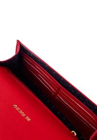 Červená peněženka s texturovaným povrchem, s více sloty na karty a tmavým interiérem vzorovaným tečkami. Zlatý branding uvnitř.