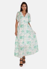 Maxiklänning i lätt, genomskinlig väv med ett blommönster i grönt och guld på en vit bakgrund. Korta volangärmar, elastisk midja.