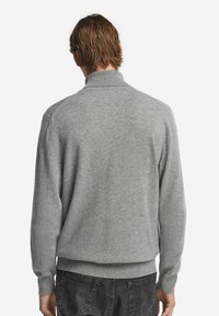 Grauer gestrickter Pullover mit hohem Kragen, gerippten Bündchen und Saum, der eine weiche Textur und einen lockeren Schnitt aufweist.