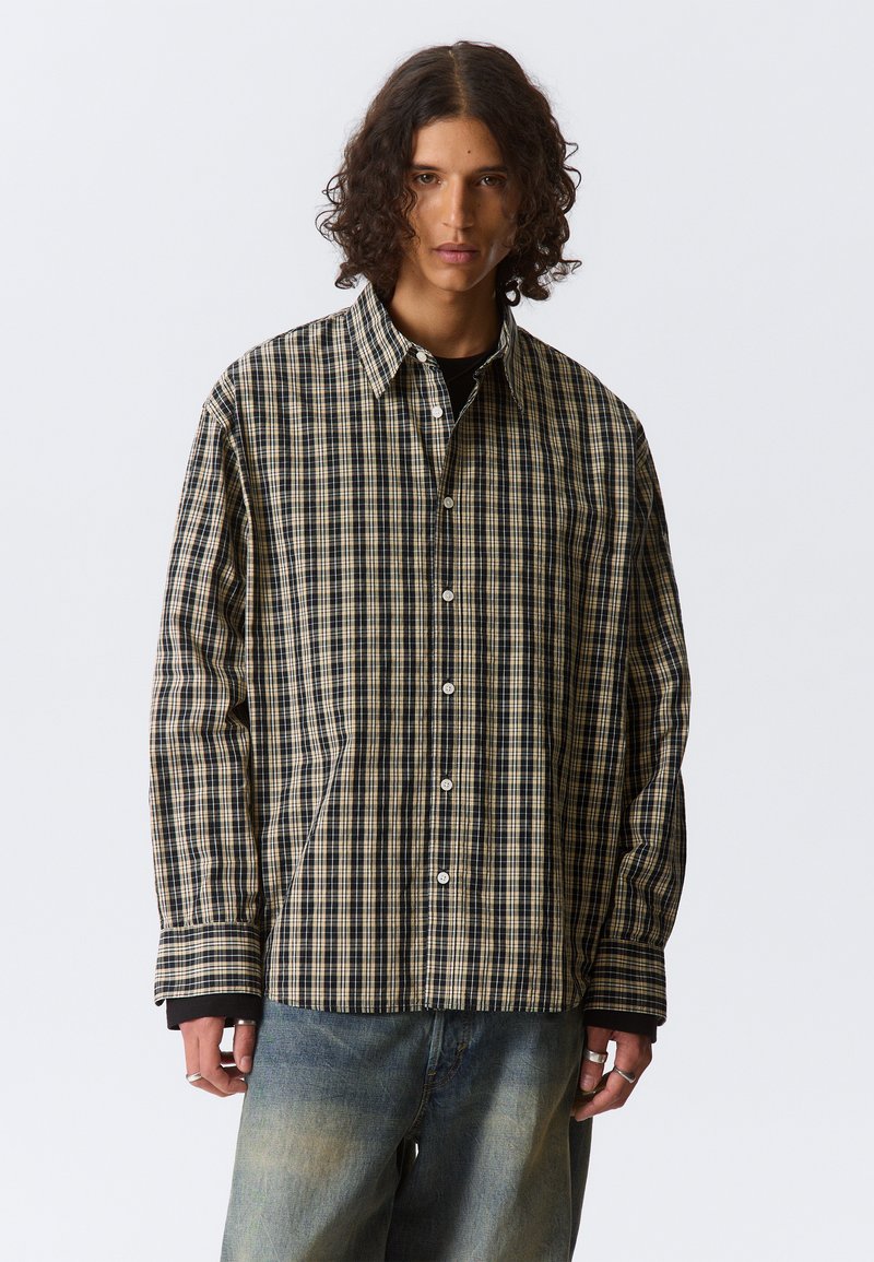 Chemise à carreaux en beige et marine avec un devant boutonné, des manches longues et des poches latérales. Fabriquée dans un tissu doux et léger.