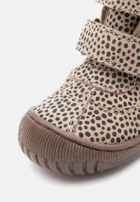 Beige gepunkteter Stoffschuh mit schwarzen Polka-Dots, ausgestattet mit zwei Klettverschluss-Riemen, Gummisohle und einer abgerundeten Spitzenform.