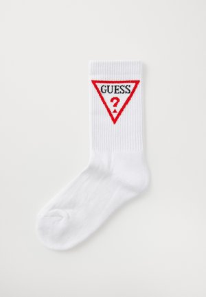Chaussette en coton blanc avec une texture côtelée, arborant un triangle rouge et le texte noir "GUESS?" imprimé sur le côté.
