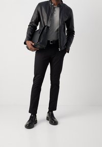 Black leather jacket, grey top with buttons, black trousers, black shoes, and holding a black bag. Sleek design and monochromatic colors.