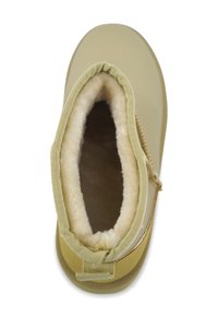 Beige laars met een zachte wolvoering en een gestructureerde buitenkant, voorzien van een elastische band bovenaan en een treklus achter voor gemakkelijk aan- en uittrekken.