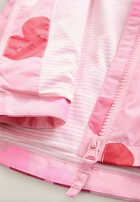 Růžová bunda s proužkovanými a jednobarevnými vzory, s uzavíráním na zip a motivy srdcí v různých odstínech růžové. Hladká textura z umělého syntetického materiálu.