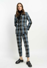 Wielokolorowy garnitur w niebieskie, czarne i beżowe paski; dopasowana marynarka z wyłogami, pasujące zwężane spodnie oraz czarne buty na platformie.