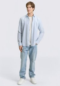 Lichtblauw overhemd over een wit T-shirt, gecombineerd met lichtblauwe spijkerbroek en witte sneakers. Het overhemd heeft een klassieke kraag en lange mouwen.