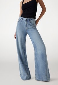 Jeans de tiro alto en denim lavado de color azul claro y pierna ancha, con un sutil detalle de desgaste y dos bolsillos frontales.