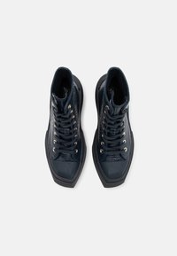 Vysoké tenisky v tmavě modrém strukturovaném materiálu s hladkým gumovým špičkou, kovovými oka a plochými tkaničkami. Rétro design s robustní podrážkou.