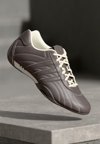 Brown leather athletic shoe with a textured upper, white laces, and striped accents. Features a smooth toe and cushioned collar.