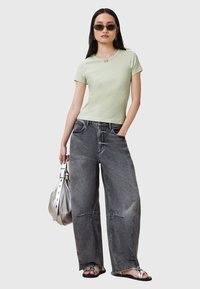 T-shirt aderente verde chiaro, jeans a gamba larga grigi con orlo sfrangiato, borsa argentata, sandali piatti e occhiali da sole rettangolari scuri.