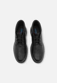 Bottines en cuir noir avec une finition texturée, présentant un bout arrondi, un design classique à lacets, et une semelle intérieure rembourrée avec un logo à l'intérieur.