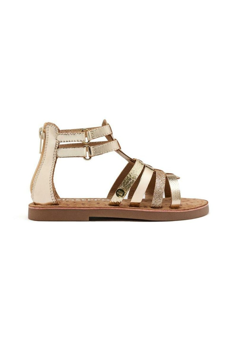 Gouden en bruine platte sandalen met meerdere metalen banden, gespen rond de enkel, een gestructureerde voetbed en een platte rubberen zool.