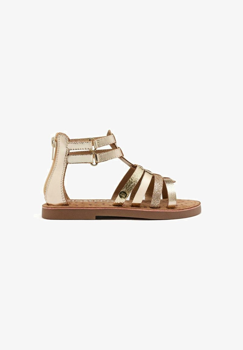 Gouden en bruine platte sandalen met meerdere metalen banden, gespen rond de enkel, een gestructureerde voetbed en een platte rubberen zool.