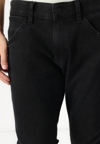 Černé džíny z denimu s hladkou texturou, designem na pět kapes a knoflíkovým zapínáním v pase. Mají šedé prošívání a jemné vyblednutí.